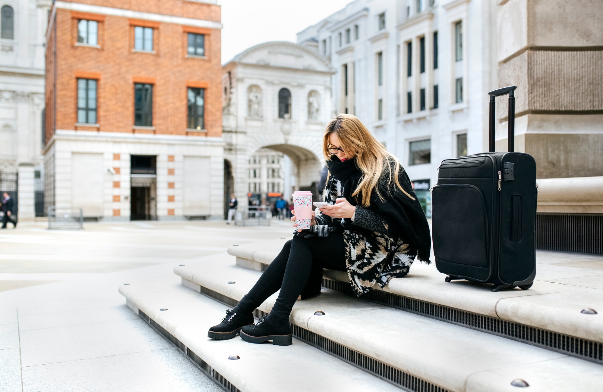 UK, London, young woman with luggage checking her cell phone on stairs